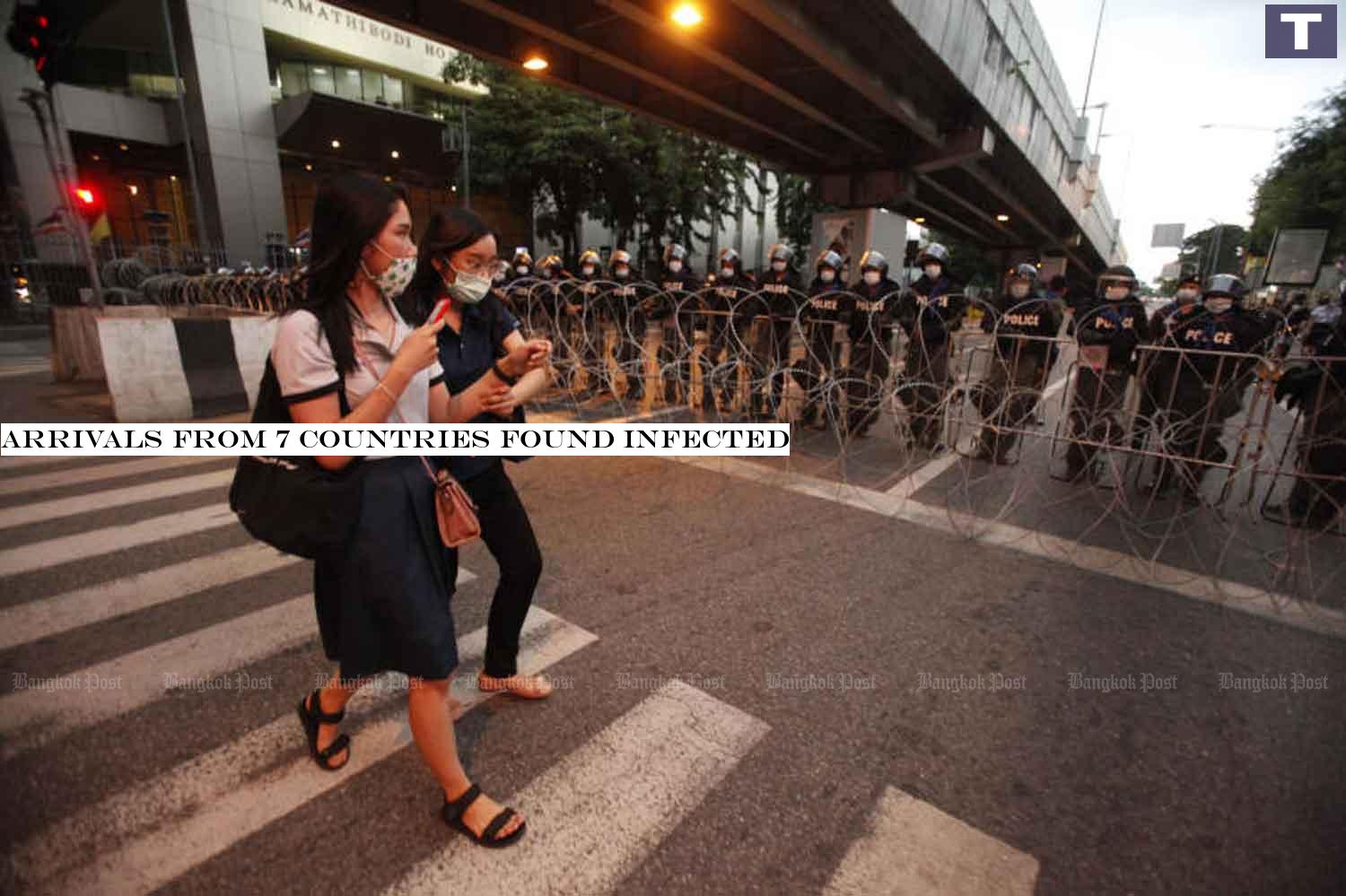 Two women in face masks walk past riot police blocking a road to Government House at Tuek Chai intersection, Bangkok, on Wednesday, when the country logged 10 new Covid-19 cases. (Photo: Pornprom Satrabhaya) Arrivals from 7 countries found infected